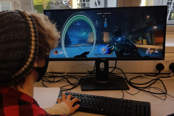 UAL Level 3 Extended Diploma In Games Development 2 The camera looks over the shoulder of a student playing a video game.