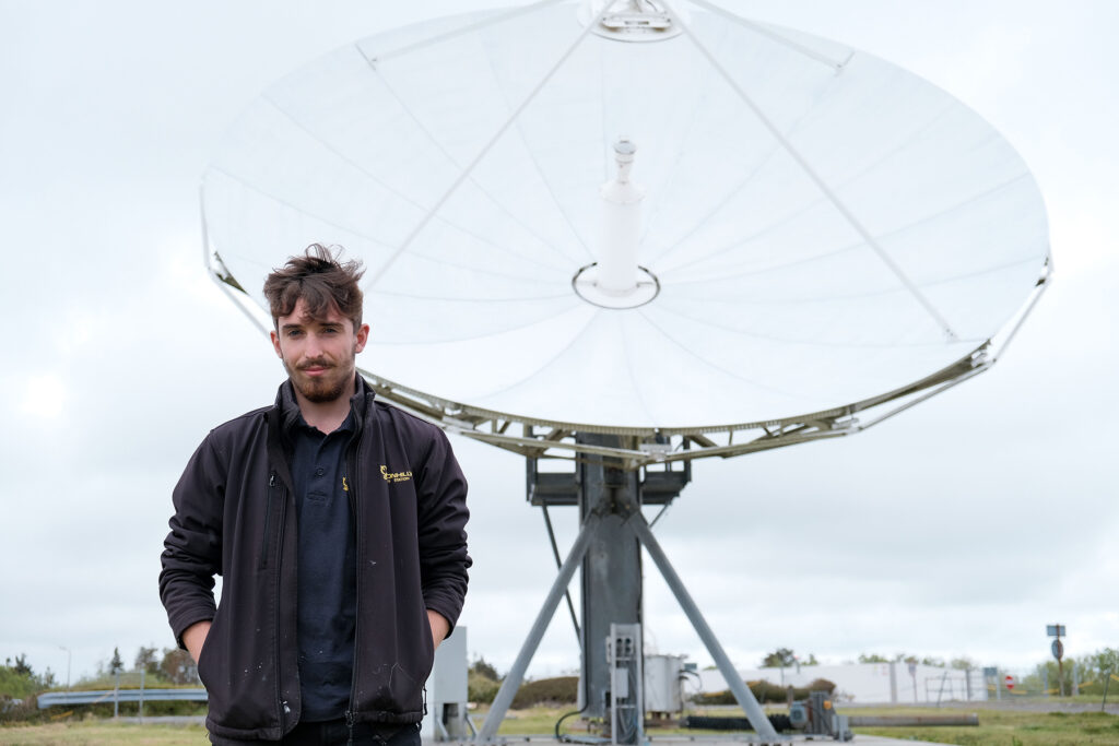 A photo of an apprentice sttod in front of a satellite dish.