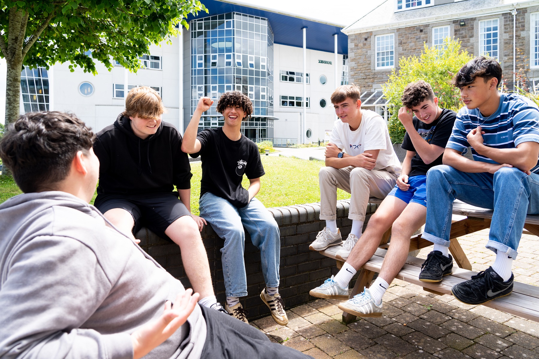 General FE PC 0008 A group of male students sit on a low wall and picnic benches. They are chatting and laughing.