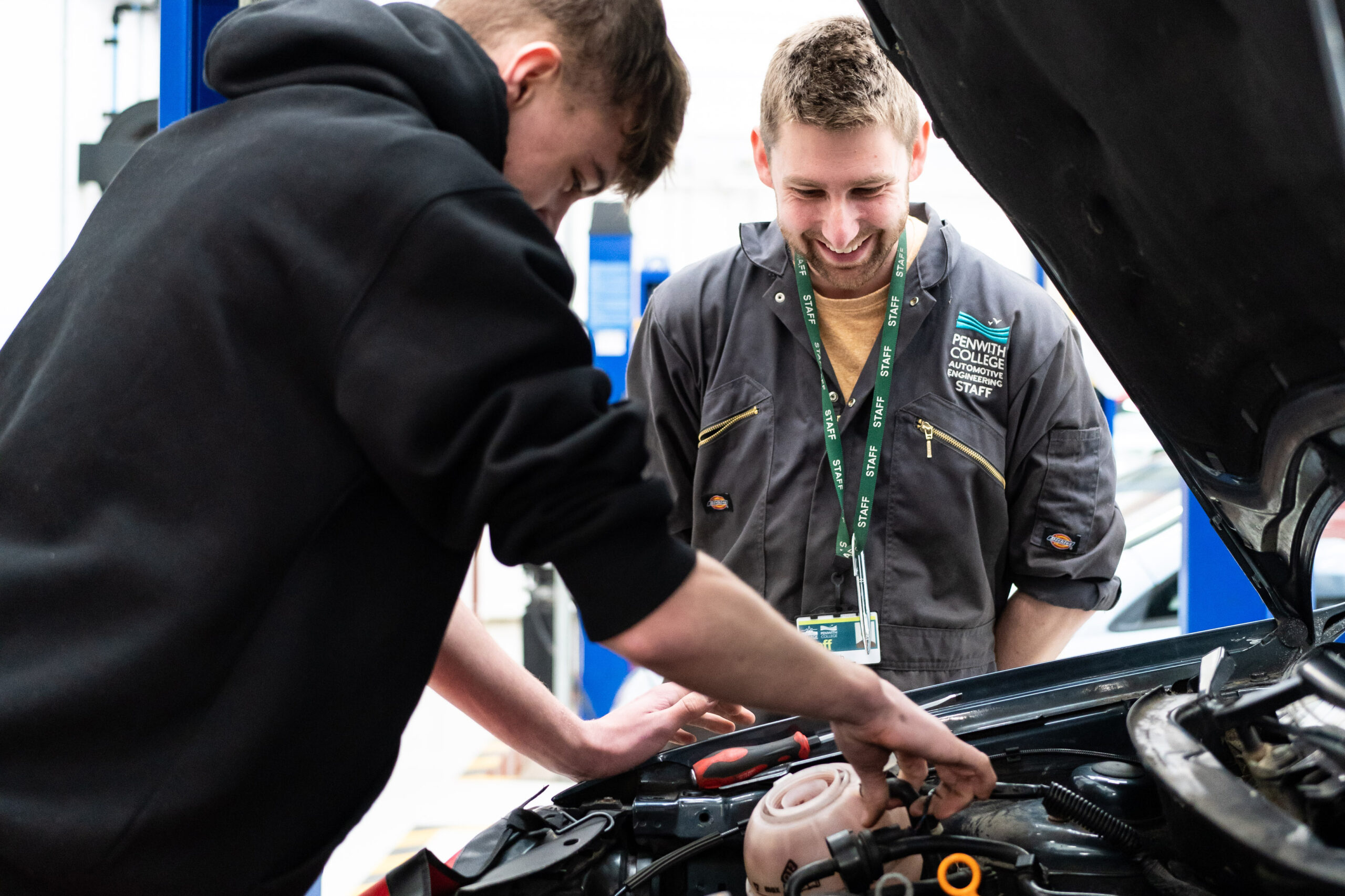 Automotive PC 0004 A tutor from the automotive department watches over a student as he works underneath the bonnet of a car.