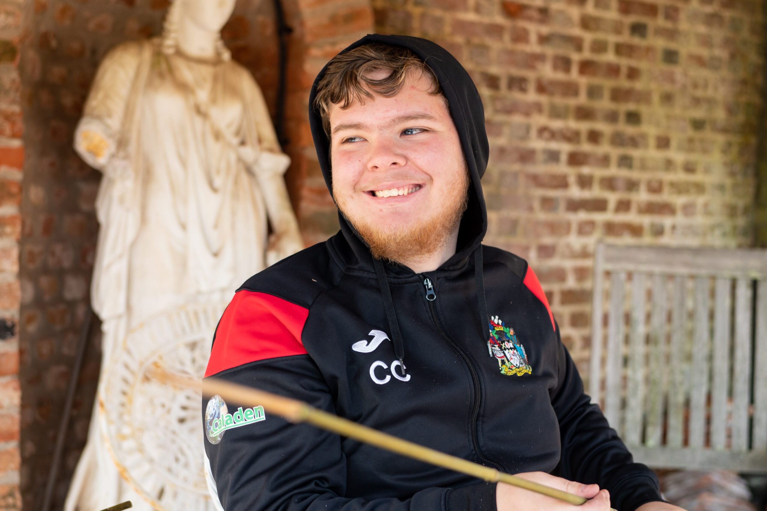 A student smiles towards something off the camera. There is a brick wall and a statue behind them.