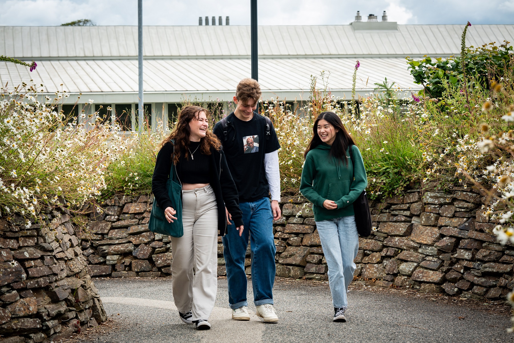 General FE TC 0043 Three students walk together side by side through the grounds of Truro campus. They laugh and smile together.