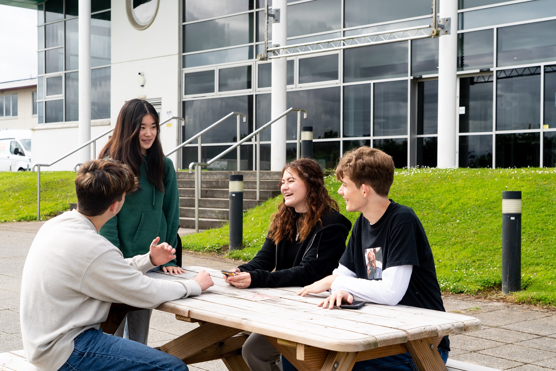 General FE TC 0051 A group of students sit at a picnice bench outside a Truro campus building chatting and laughing.