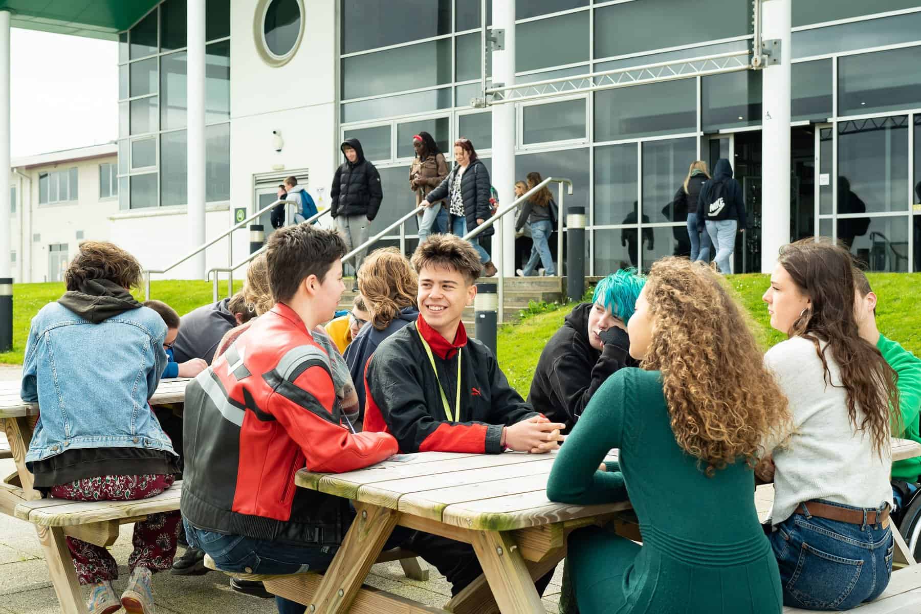 General FE TC 060 A group of students sit outside on picnic benches in front of the Lynher building at Truro College.