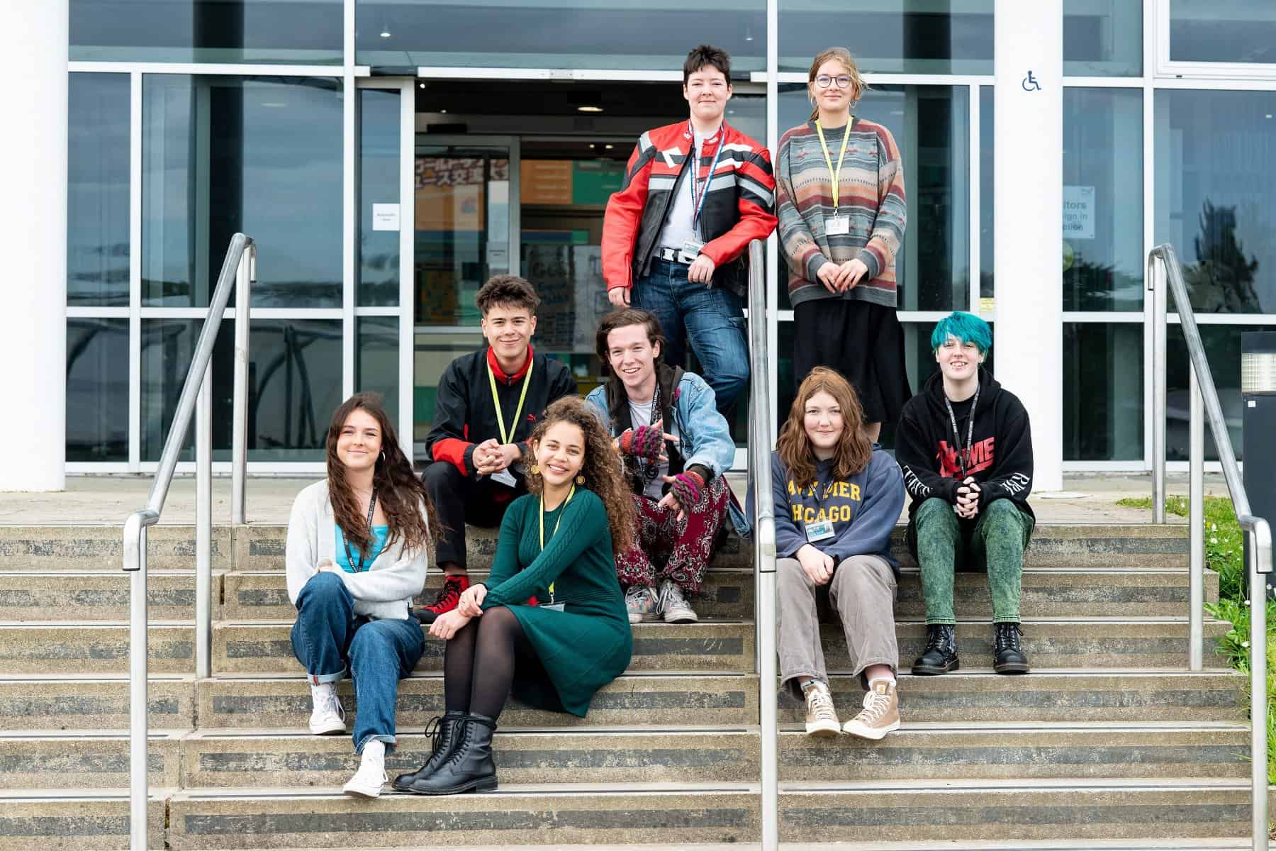 General FE TC 062 A group of students sit on the steps outside the Lynher building. They all smile at the camera.