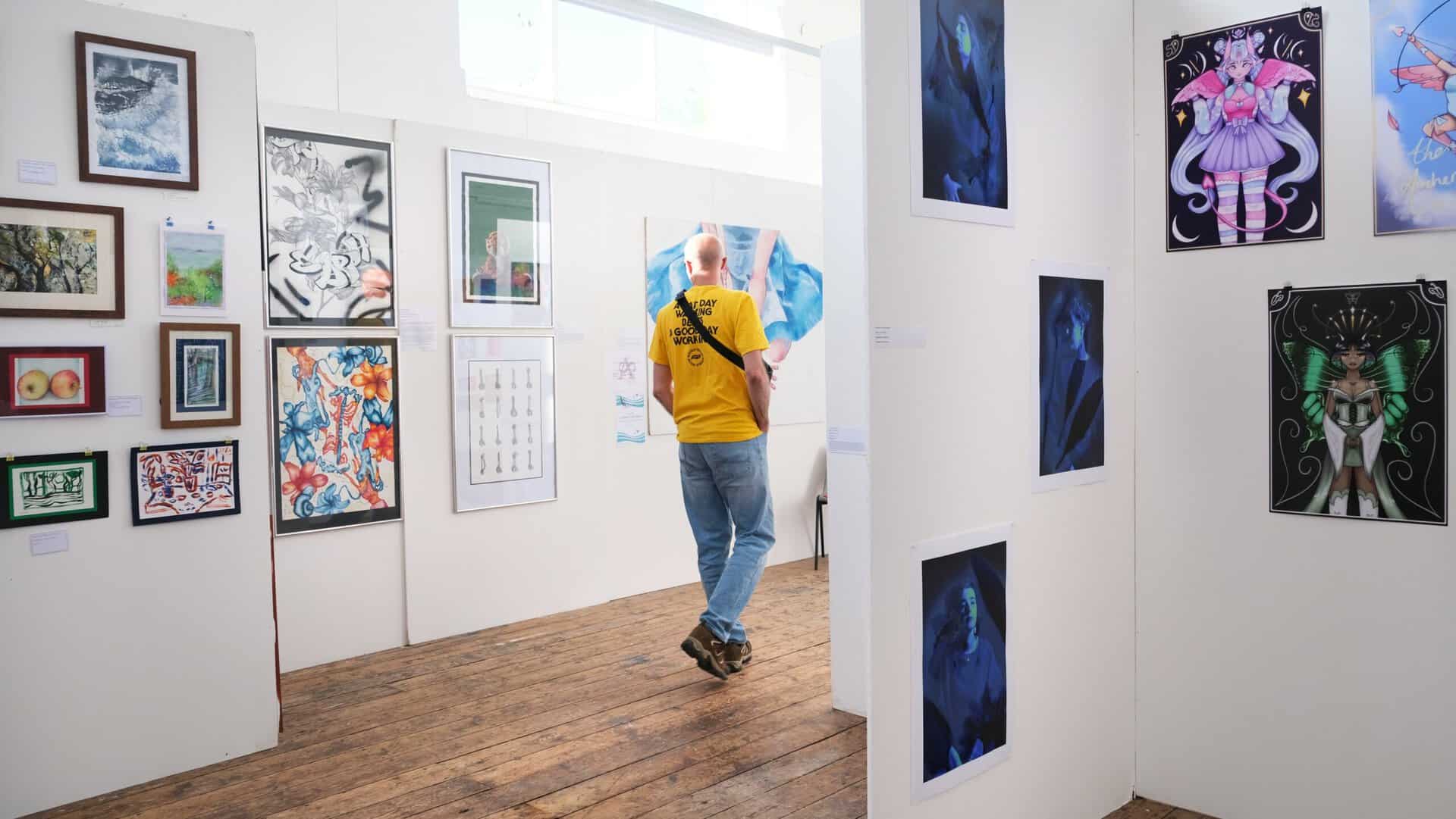 Illuminate Man in yellow tshirt, walks through the gallery walls of artwork.